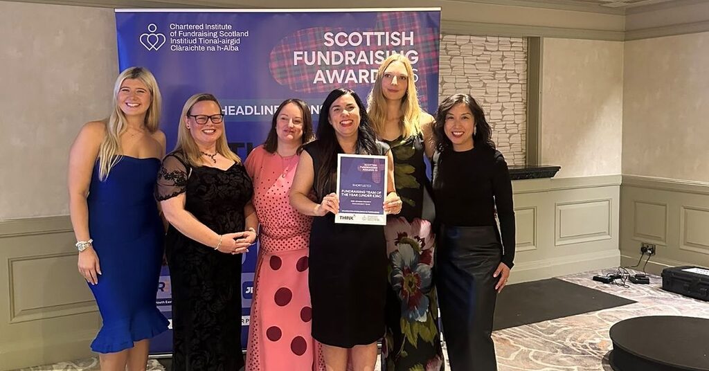 The NHS Lothian Charity Engagement Team holding their runners up plaque in front of a Scottish Fundraising Awards banner
