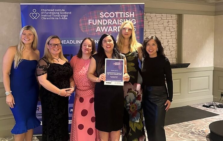 The NHS Lothian Charity Engagement Team holding their runners up plaque in front of a Scottish Fundraising Awards banner