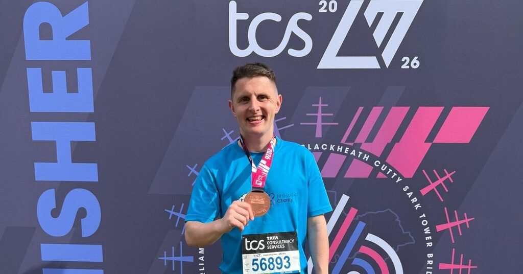 Ross Winton standing in front of the TCS London Marathon backdrop with his finishers medal